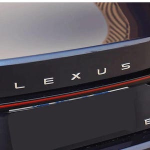 Puede incluir: La parte trasera del maletero de un vehículo Lexus azul oscuro con las letras metálicas plateadas L E X U S centradas sobre una fina barra de luz roja horizontal. A la derecha, la designación del modelo ES 200 en metal plateado es visible.