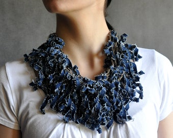 May include: A white t-shirt with a blue denim necklace. The necklace is made of strips of denim fabric that have been frayed and knotted together.