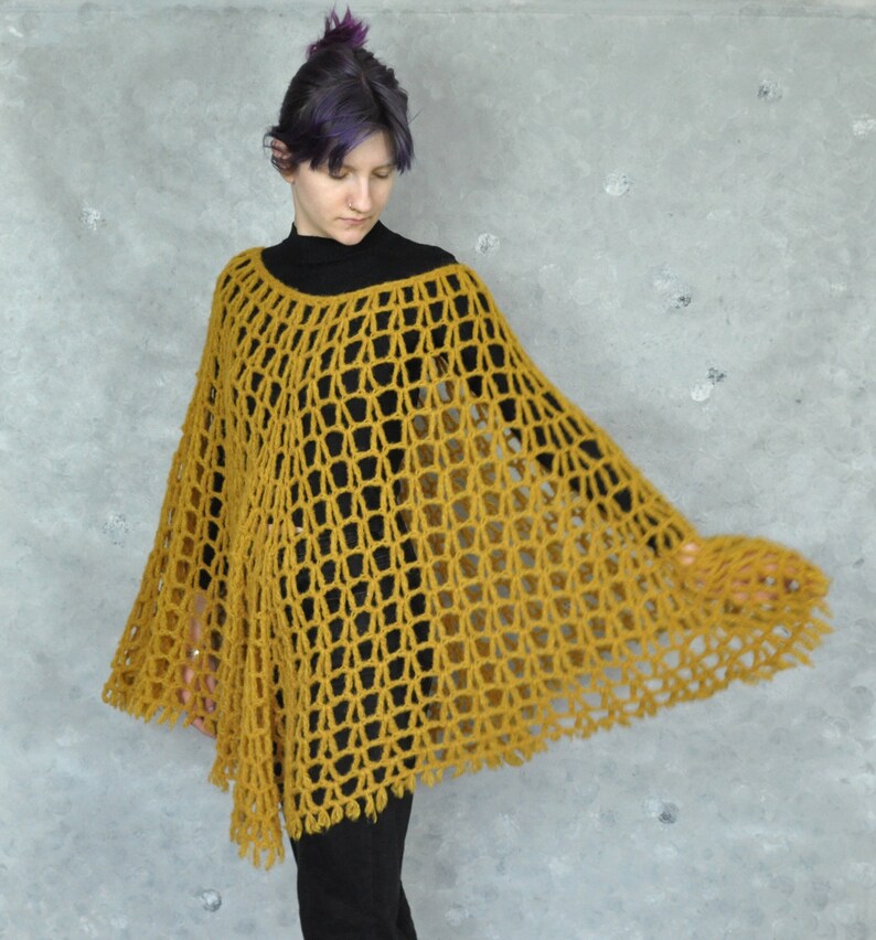 Peut inclure: Un poncho en crochet jaune moutarde avec un motif ajour&eacute; en dentelle. Le poncho a une forme ample et fluide et un ourlet frang&eacute;.