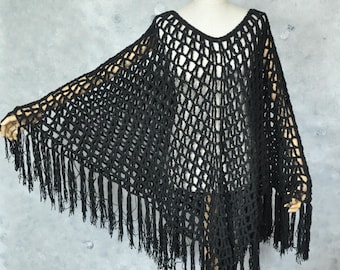 Peut inclure: Un poncho noir en crochet à col en V et longues franges. Le poncho est présenté sur un mannequin, mettant en valeur son design drapé et sa texture. Les franges pendent le long du bord inférieur.