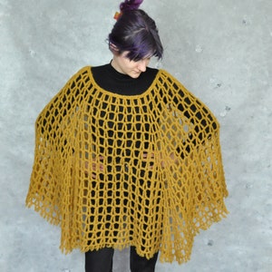 Peut inclure: Un poncho en crochet jaune moutarde &agrave; la maille l&acirc;che et ouverte. Le poncho a une bordure en franges et est port&eacute; par une personne aux cheveux violets.