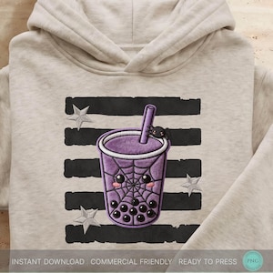 Puede incluir: Una sudadera con capucha de color beige que presenta un gráfico de un vaso de té de burbujas morado con un patrón de telaraña, una pequeña araña en la pajita y una cara linda. El diseño está sobre rayas negras horizontales y estrellas grises.