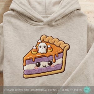 May include: A beige hooded sweatshirt featuring a central graphic of a slice of pie with a purple and white layered filling, topped with orange icing, a small white ghost, and candy corn pieces, all rendered in a textured, embroidered style.