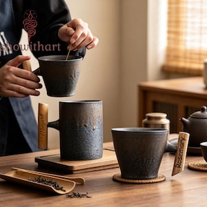 May include: Three dark gray ceramic mugs with textured surfaces and light wood handles. Two handles feature engraved names, Margaret and Rosemary. The mugs have a rustic, mottled finish with a drip-like glaze pattern near the top rim.
