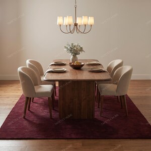 May include: A dining room set featuring a rectangular wooden table, six beige upholstered chairs, and a burgundy rug. A bronze chandelier hangs above the table, and a vase of flowers and a bowl of fruit are on the table.