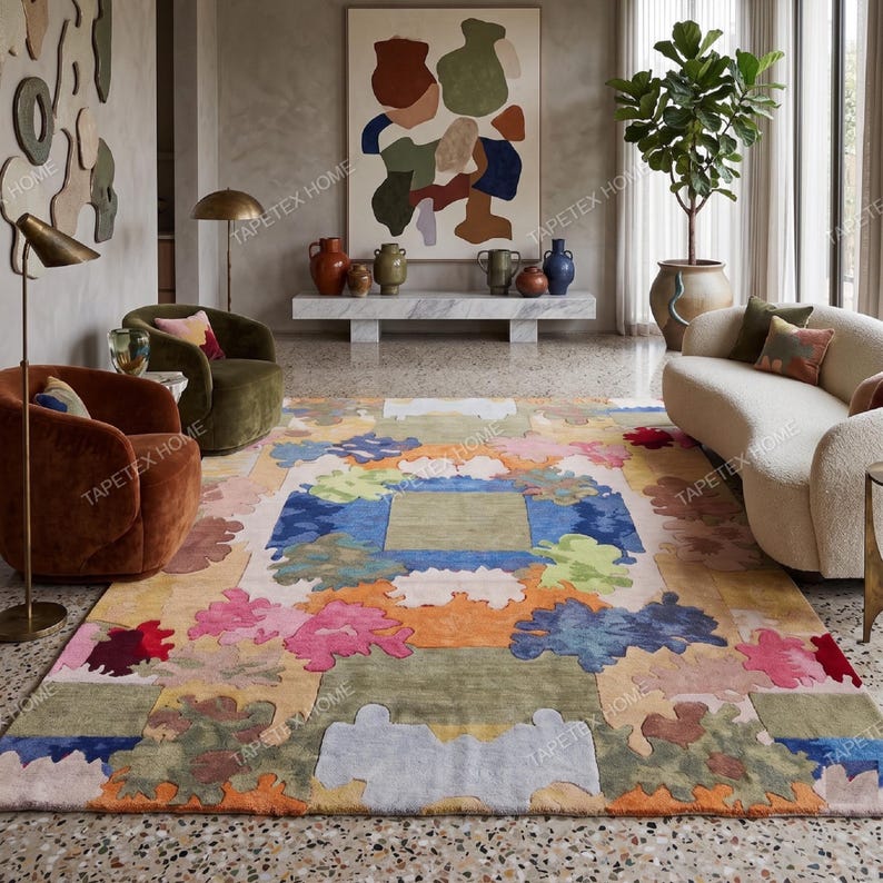 Puede incluir: Una gran alfombra colorida con un dise&ntilde;o floral abstracto. La alfombra presenta una mezcla de colores que incluyen azul, rosa, naranja y verde. La habitaci&oacute;n tambi&eacute;n incluye un sof&aacute; blanco, dos sillones y una gran pintura.