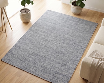 May include: A rectangular area rug featuring a textured, woven surface in a deep charcoal grey colour. The rug has a consistent, dense weave pattern throughout its entire surface, creating a uniform appearance that lies flat on the wooden floor.
