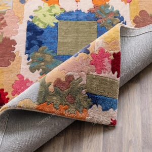 Puede incluir: Una colorida alfombra con un dise&ntilde;o floral. La alfombra presenta una mezcla de colores que incluyen azul, verde, rosa, naranja y marr&oacute;n. La alfombra est&aacute; parcialmente enrollada, revelando el reverso gris y la textura de la alfombra.