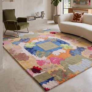 Puede incluir: Una colorida alfombra con un dise&ntilde;o abstracto &uacute;nico. La alfombra presenta un cuadrado central rodeado por un borde de varias formas y colores, incluyendo azul, verde, naranja y rosa. La alfombra est&aacute; colocada en un sal&oacute;n.