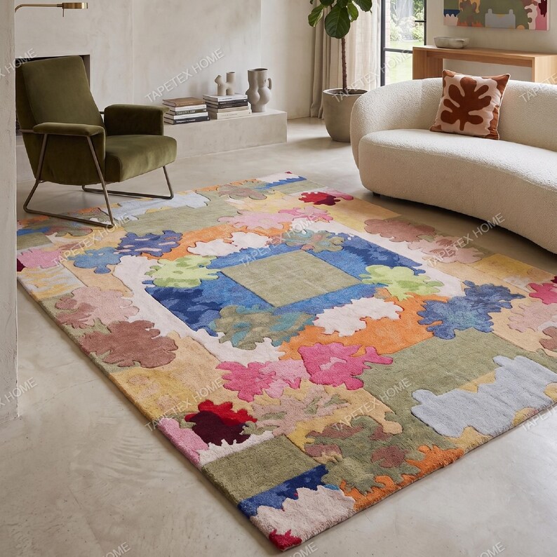 Puede incluir: Una colorida alfombra con un dise&ntilde;o abstracto &uacute;nico. La alfombra presenta un cuadrado central rodeado por un borde de varias formas y colores, incluyendo azul, verde, naranja y rosa. La alfombra est&aacute; colocada en un sal&oacute;n.