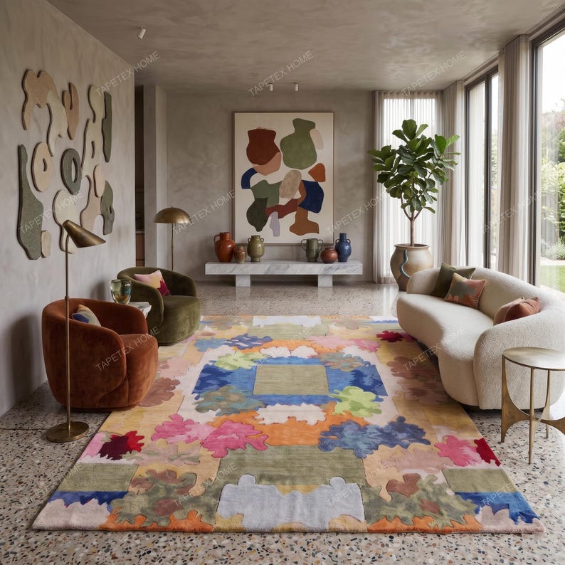 Puede incluir: Una colorida alfombra abstracta con un dise&ntilde;o geom&eacute;trico. La alfombra presenta una mezcla de colores pastel, incluyendo rosa, azul, naranja y verde. Se encuentra en un sal&oacute;n moderno con un sof&aacute; blanco y dos sillones.