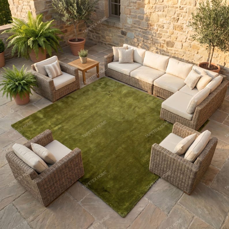 May include: Outdoor patio furniture set with a large green rug. The set includes a sectional sofa, two armchairs, and a small wooden table. The furniture has woven wicker frames and beige cushions.