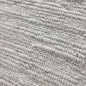 May include: Close-up of a textured, light gray rug. The rug has a ribbed pattern with a soft, plush appearance. The fibers are tightly woven, creating a durable and comfortable surface. The neutral color makes it suitable for various interior design styles.