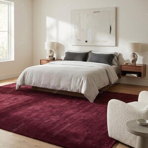 May include: A bedroom scene featuring a large bed with a light-colored comforter and dark gray pillows. A deep red rug covers the floor. Two wooden nightstands with lamps flank the bed. A large abstract painting hangs above the bed.