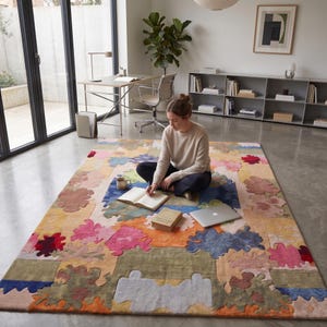 Puede incluir: Una colorida alfombra con un dise&ntilde;o de patchwork. La alfombra presenta una variedad de formas y colores, incluyendo rosa, azul, naranja y verde. Una persona est&aacute; sentada en la alfombra con un libro y un port&aacute;til.