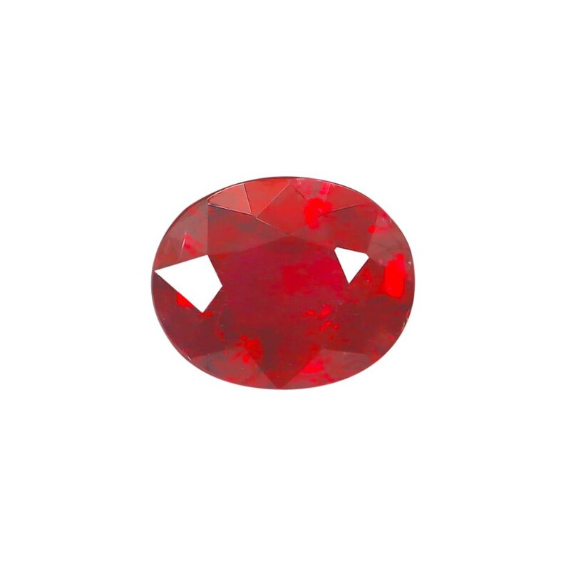 May include: A faceted, oval-shaped, deep red gemstone. The gem has a polished surface with multiple facets that reflect light. The color is a rich, saturated red, with some lighter areas. The gemstone is set against a white background.