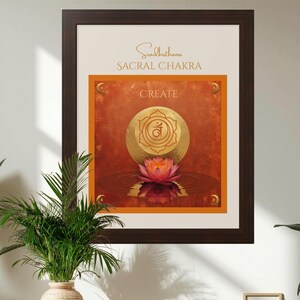 May include: A framed wall art print featuring the Sacral Chakra, labeled Svadhisthana and CREATE. The artwork displays a golden circular symbol above a pink lotus flower on a textured orange background, all enclosed in a dark brown frame.