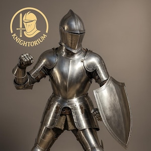 Puede incluir: Armadura completa de acero pulido, que incluye casco, peto y perneras. La armadura se completa con un escudo y está diseñada para la protección en combate. La imagen incluye el logotipo de Knightorium.