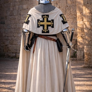 May include: A full suit of medieval armor, including a helmet with decorative silver horns, chainmail, and a white tunic with a gold cross emblem. The knight is holding a long sword. The image is taken outdoors.