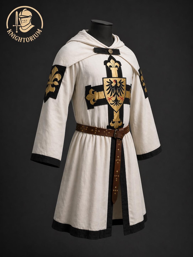 May include: A white medieval tunic with black trim, a hood, and a brown leather belt. The tunic features a gold cross design with a black eagle emblem and gold fleur-de-lis accents. The Knightorium logo is in the upper left corner.