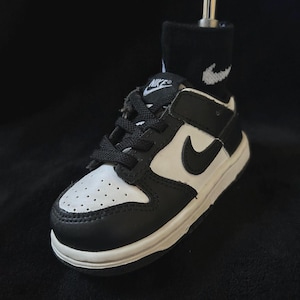 May include: A black and white Nike Dunk Low sneaker with a white midsole. The shoe has a black swoosh and laces. A black sock with a white Nike logo is inside the shoe.