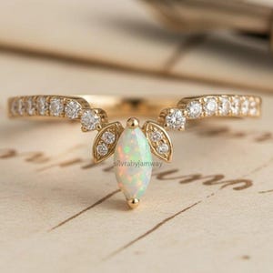 May include: A gold ring featuring a marquise-cut opal and small diamonds. The ring has a distinctive, curved design with diamond accents. The opal is a light, iridescent colour, and the ring is set on a vintage-style background.