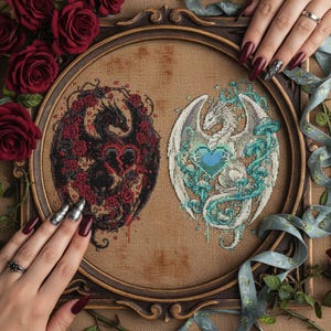 May include: Two framed cross-stitch artworks featuring dragons. One dragon is black, surrounded by red roses and a heart. The other is white, with blue accents and a heart. The frames are brown, with a floral and ribbon background.