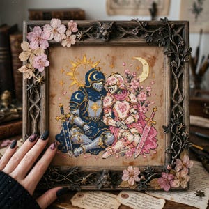 May include: A cross-stitch embroidery featuring two knights in armour, one in blue and one in pink, sitting together under a sun and moon. The piece is displayed in a dark, ornate, carved wooden frame decorated with small pink cherry blossoms.