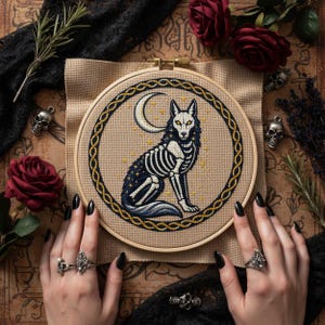 This gothic cross-stitch pattern features a skeletal fox seated beneath a glowing crescent moon, surrounded by a decorative Celtic-style ring and shimmering stars. The fox’s elegant bone structure is rendered in soft ivory and pale gray tones, contrasted against a deep blue night sky dotted with golden starlight. The circular framing gives the design a symbolic, talisman-like presence, making it perfect for gothic décor, fantasy art collections, and celestial-themed embroidery displays.