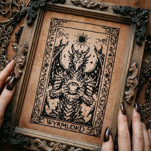 May include: A framed cross-stitch featuring a black and white design of a dragon-like creature with the text "WYRMLORD" at the bottom. The frame is ornate, dark wood. The background is a tan fabric.