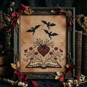 Puede incluir: Arte de punto de cruz enmarcado con un diseño gótico. La obra representa tres murciélagos volando sobre un diseño en forma de corazón con flores y un libro abierto. La paleta de colores incluye negro, rojo y dorado sobre un fondo beige. El marco marrón oscuro tiene cintas burdeos.