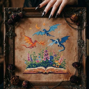 Puede incluir: Arte de punto de cruz que representa tres dragones volando sobre un libro abierto con flores coloridas. Los dragones son en tonos naranja y azul, con una luna y estrellas en el fondo. Enmarcado en un marco de madera decorativo.