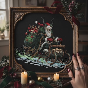 May include: Cross-stitch art of a dark Santa Claus in a sleigh pulled by skulls, carrying a sack of skulls and ornaments. The artwork is framed in a decorative wooden frame with a dark background. The image is decorated with candles and ornaments.