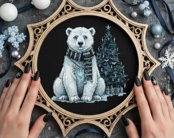 May include: Cross-stitch embroidery of a polar bear wearing a scarf, with a Christmas tree in the background. The artwork is framed in a decorative, ornate, gold-colored hoop. The bear is white with blue accents.