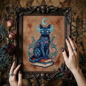 May include: Cross-stitch art of a black cat with blue and pink floral accents, sitting atop books. The cat has a crescent moon above its head and is framed in a dark wooden frame with skull and thorn details. The artwork is held by hands with long, dark nails.