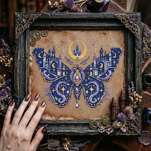 Peut inclure: Broderie au point de croix d'un papillon avec des ailes en forme de château, une lune et des étoiles. Le motif est en bleu, violet et or, encadré dans un cadre en bois foncé avec des détails d'angle ornés.