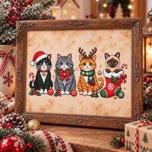 Puede incluir: Un bordado en punto de cruz enmarcado que muestra cuatro gatos con atuendos festivos. Un gato blanco y negro lleva un gorro de Papá Noel, uno gris tiene una corona verde, un atigrado naranja lleva astas de reno y un siamés está dentro de un calcetín rojo.