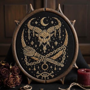 May include: A framed, round cross-stitch featuring a gold-colored goat skull, crescent moon, stars, and a broom on a black background. The frame is dark brown with decorative points. The artwork has a gothic or witchy theme.