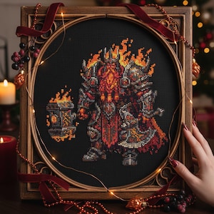 May include: A framed cross-stitch depicting a fantasy warrior with fiery details. The artwork features a character in armor, holding a hammer and axe, with flames emanating from the head and weapons. The frame is wooden with a dark finish.