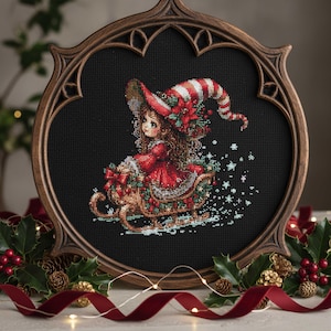 May include: A framed cross-stitch featuring a girl in a red dress and hat riding a sleigh. The sleigh is decorated with holly and bows. The frame is dark brown and oval-shaped, with a decorative border. The background is black.