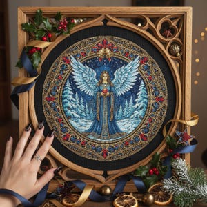 Puede incluir: Un bordado enmarcado que representa un ángel con grandes alas de color azul claro, sosteniendo un corazón rojo. La obra de arte está ambientada en una escena de bosque invernal con un cielo estrellado, enmarcada en un marco de madera de estilo gótico. Acebo decorativo y cintas rodean el marco.