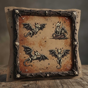 May include: Cross-stitch art showing four skeletal dragons with black wings on a tan background. The artwork is framed in a dark brown, ornate wooden frame with skull and bat details. The piece is displayed on a wooden surface.