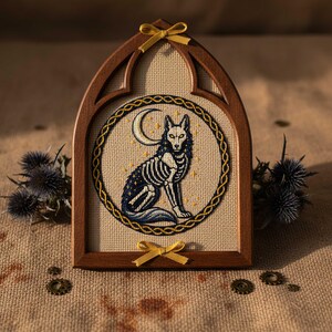 This gothic cross-stitch pattern features a skeletal fox seated beneath a glowing crescent moon, surrounded by a decorative Celtic-style ring and shimmering stars. The fox’s elegant bone structure is rendered in soft ivory and pale gray tones, contrasted against a deep blue night sky dotted with golden starlight. The circular framing gives the design a symbolic, talisman-like presence, making it perfect for gothic décor, fantasy art collections, and celestial-themed embroidery displays.