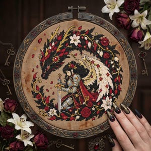 Puede incluir: Un bastidor de bordado circular con un diseño de punto de cruz de un caballero alado con armadura arrodillado con una espada, rodeado por un dragón negro, rosas rojas y lirios blancos sobre tela beige. El marco es de metal oscuro ornamentado.