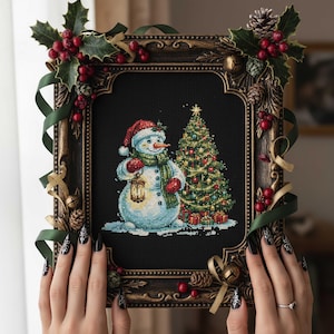 Può includere: Un ricamo incorniciato con un pupazzo di neve con naso a carota, cappello, sciarpa e guanti rossi, che tiene una lanterna. Un albero di Natale decorato e regali sono accanto al pupazzo di neve. La cornice è decorata con agrifoglio, bacche e nastri.