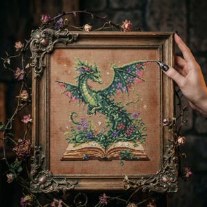 May include: A framed cross-stitch of a green dragon with floral accents, wings, and tail. The dragon is emerging from an open book filled with flowers. The frame is ornate, with a floral design, and is surrounded by dried flowers and thorns.
