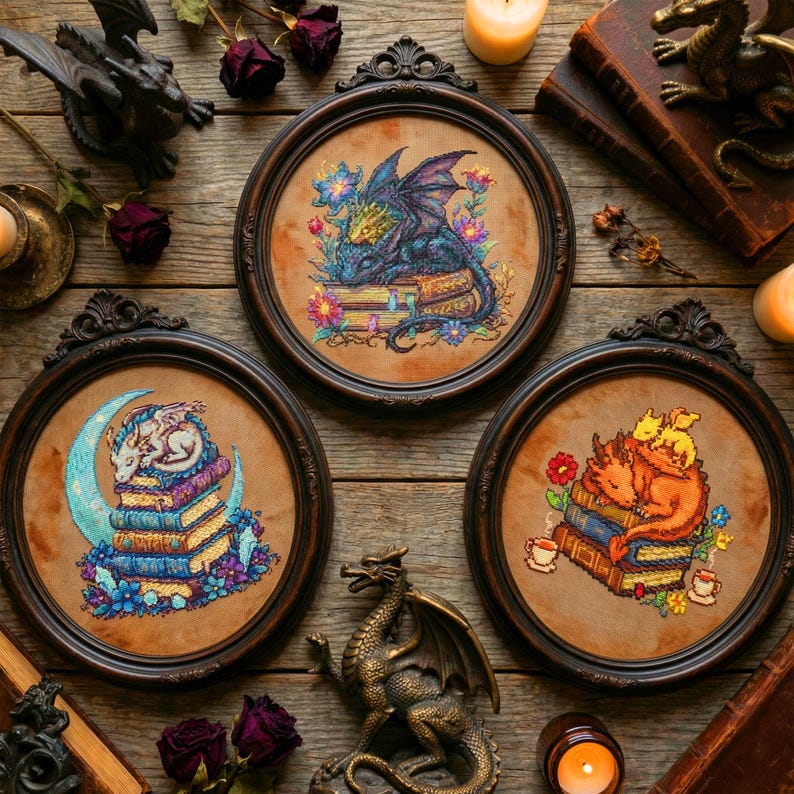 Puede incluir: Tres obras de arte en punto de cruz enmarcadas con dragones. Una muestra un drag&oacute;n azul sobre libros, otra un drag&oacute;n blanco sobre una luna creciente y la tercera un drag&oacute;n naranja con dos dragones m&aacute;s peque&ntilde;os. Cada una est&aacute; rodeada de flores.