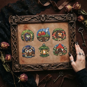 May include: A framed cross-stitch sampler featuring six whimsical scenes. Each scene depicts a small, round dwelling with a different animal or creature, including a frog, fox, and owl. The frame is dark brown with ornate carvings of gargoyles.