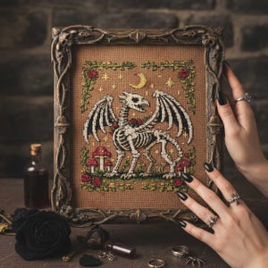Könnte beinhalten: Kreuzstich-Kunstwerk mit einem Skelettdrachen mit schwarz-weißen Flügeln, umgeben von roten Rosen, Pilzen und einem Mond. Das Kunstwerk ist in einem verzierten braunen Rahmen gefasst, passend für gotische oder Fantasy-Dekorationen.