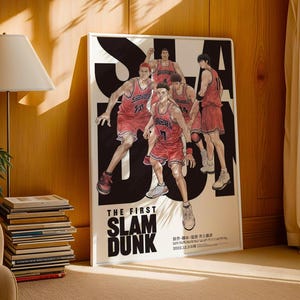 Puede incluir: Un póster enmarcado que presenta un equipo de baloncesto con uniformes rojos sobre un fondo en blanco y negro. El texto "THE FIRST SLAM DUNK" es visible. El póster está apoyado contra una pared de madera.